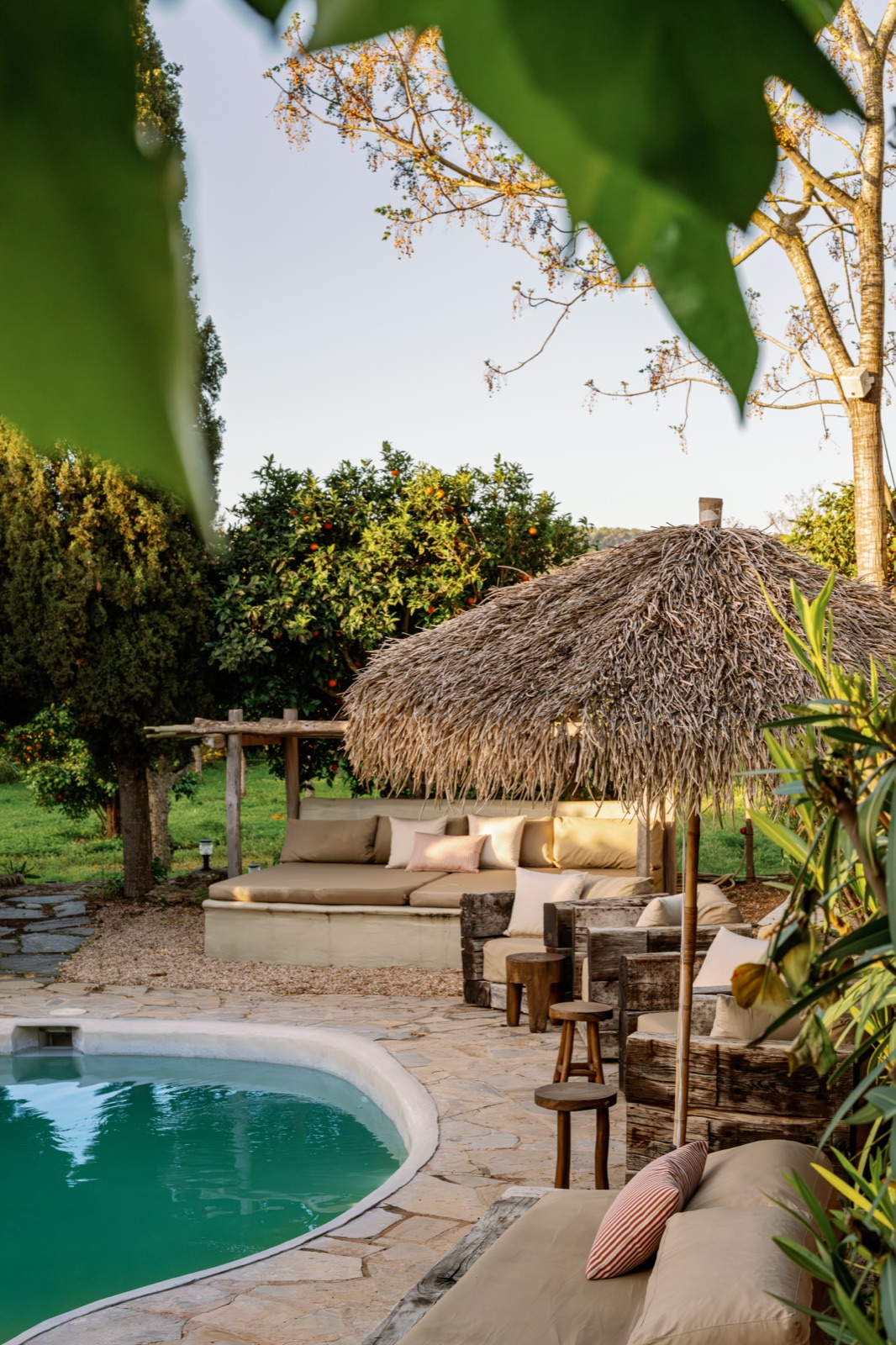 Zona de piscina con sombrilla de paja en el hotel boutique Can Sastre, hora dorada